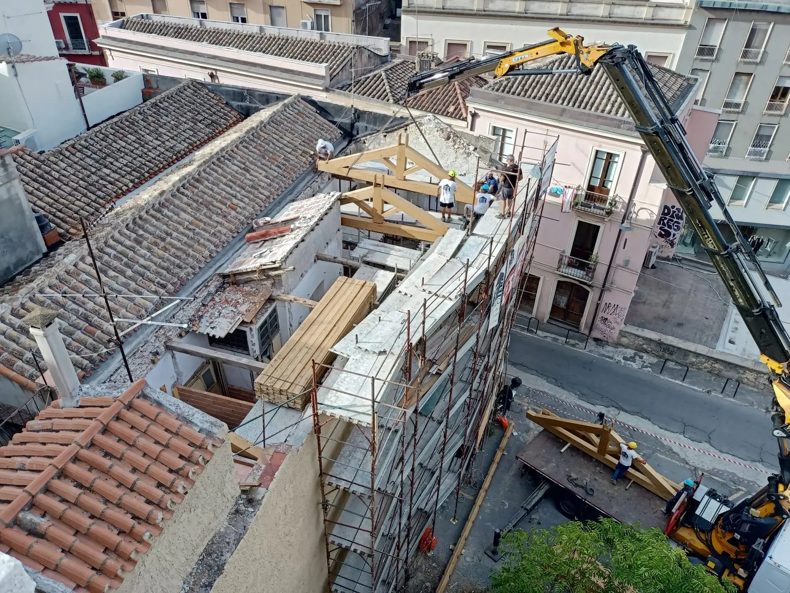 Una gru cala una capriata di legno sul tetto scoperchiato, tra i coppi del centro storico di Cagliari