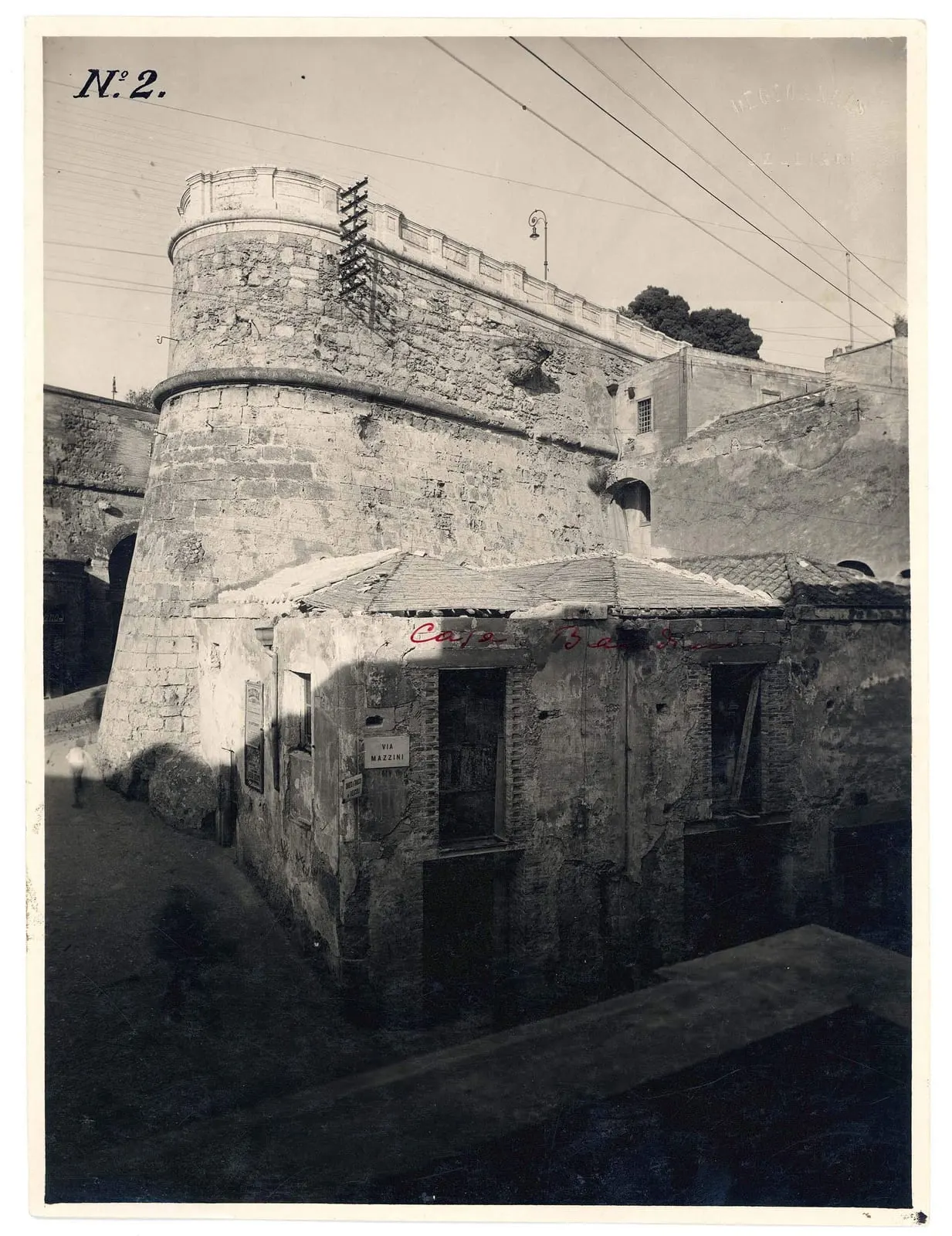 Fotografia d'epoca dell'edificio addossato alla torre bastionata, con la targa stradale Via Mazzini leggibile sull'angolo